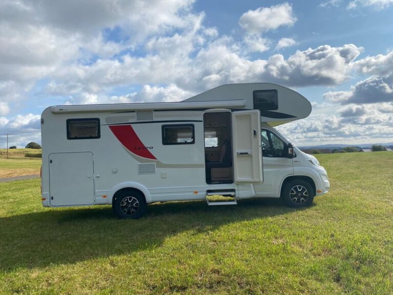 Weser-Vermietung: Wohnmobil, Boot & Motorrad mieten an der Weser 9 Weißes Bürstner Lyseo Wohnmobil mit ausgefahrener Markise und offener Tür auf grünem Gras unter blauem Himmel mit weißen Wolken.